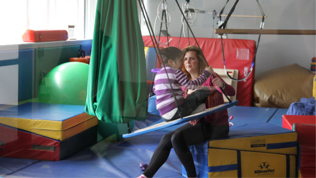 Woman with a child in a playroom helping her on a swing.
