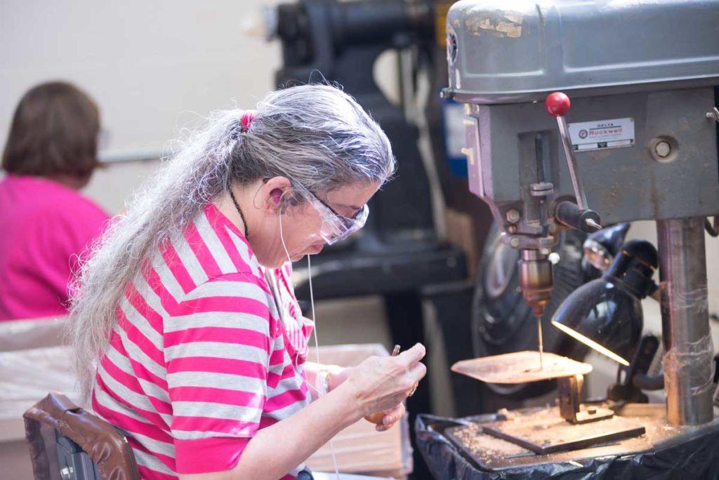 A woman works with a drill bit while listening to headphones.