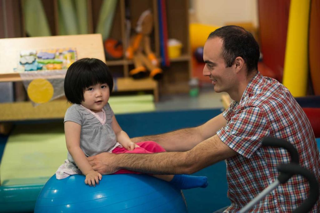 A man holds a baby girl on an exercise ball.