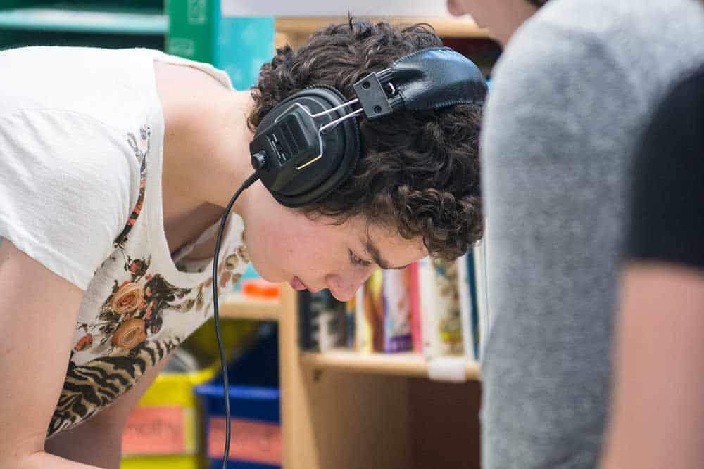 A boy wears headphones while placing shaped into a yellow frame.