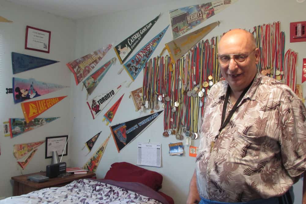 A man stares at the camera with several flags on the wall behind him.