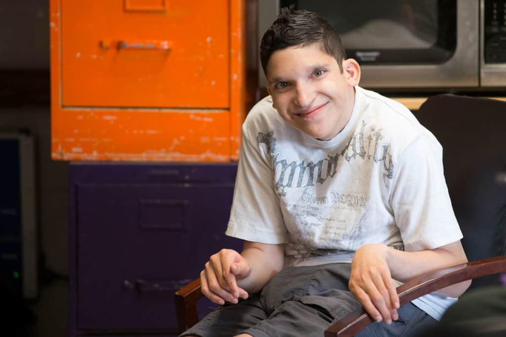 A boy sits in a chair smiling.